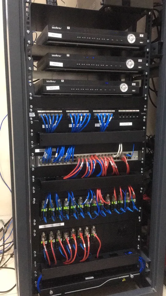 Rack com gravadores Intelbras, patch panel e cabos azuis e vermelhos organizados